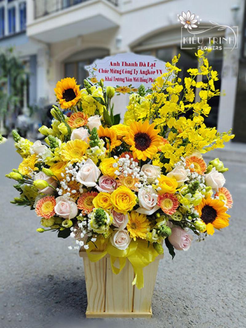 Một lẵng hoa khai trương lớn với sự kết hợp của hoa hướng dương, hoa đồng tiền, và các loại hoa màu đỏ, vàng khác, thể hiện sự chúc mừng và mong cầu tài lộc